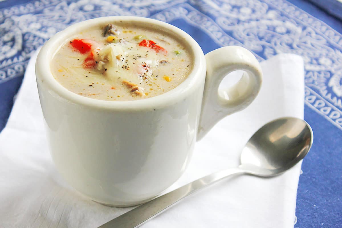 Creamy chicken and vegetable soup with a spoon on the side.