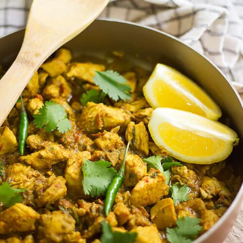 Chicken karahi in a pan with two slices of lemon on the side.