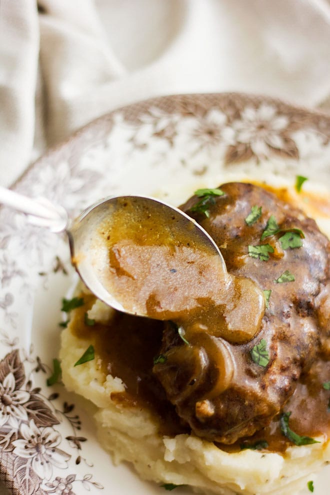 Pouring gravy over salisbury steak.