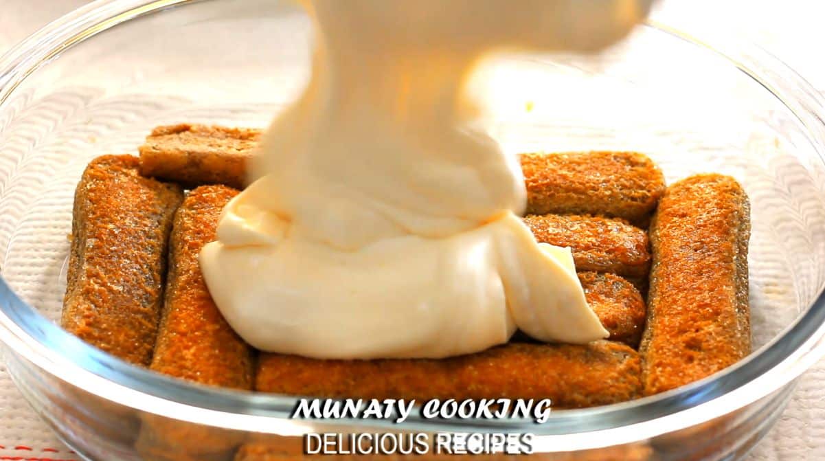 Adding a layer of cream and egg yolks over ladyfinger.