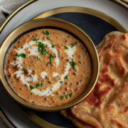 dal makhani served in a black and golden bowl with paratha.