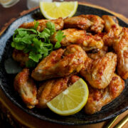 Chicken wings made in an Air Fryer and served on a black plate with lemon slices.