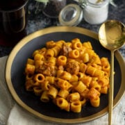 Libyan mbakbaka Pasta with meat cubes, served on a black plate.