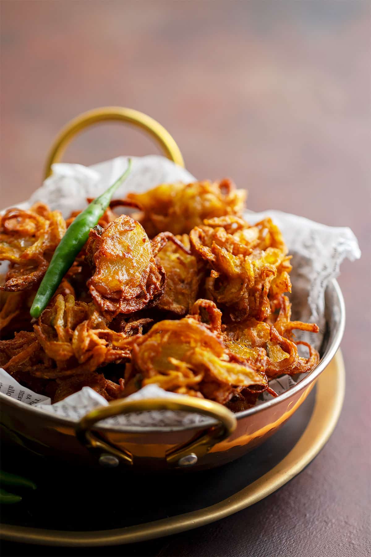 Close up image of onion pakora served on parchemnt paper in a bowl.