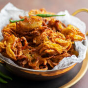 Crispy onion pakora served in a bowl with green chili.