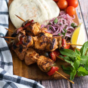 Grilled shish tawook served on a peice of wook with vegetables on the side.