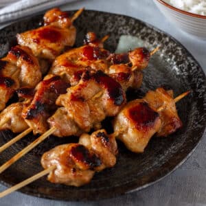 Teriyaki chicken skewers served on a black plate.
