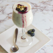 Freekeh pudding with blueberry sauce, served in a tall glass, garnished with pistachios.
