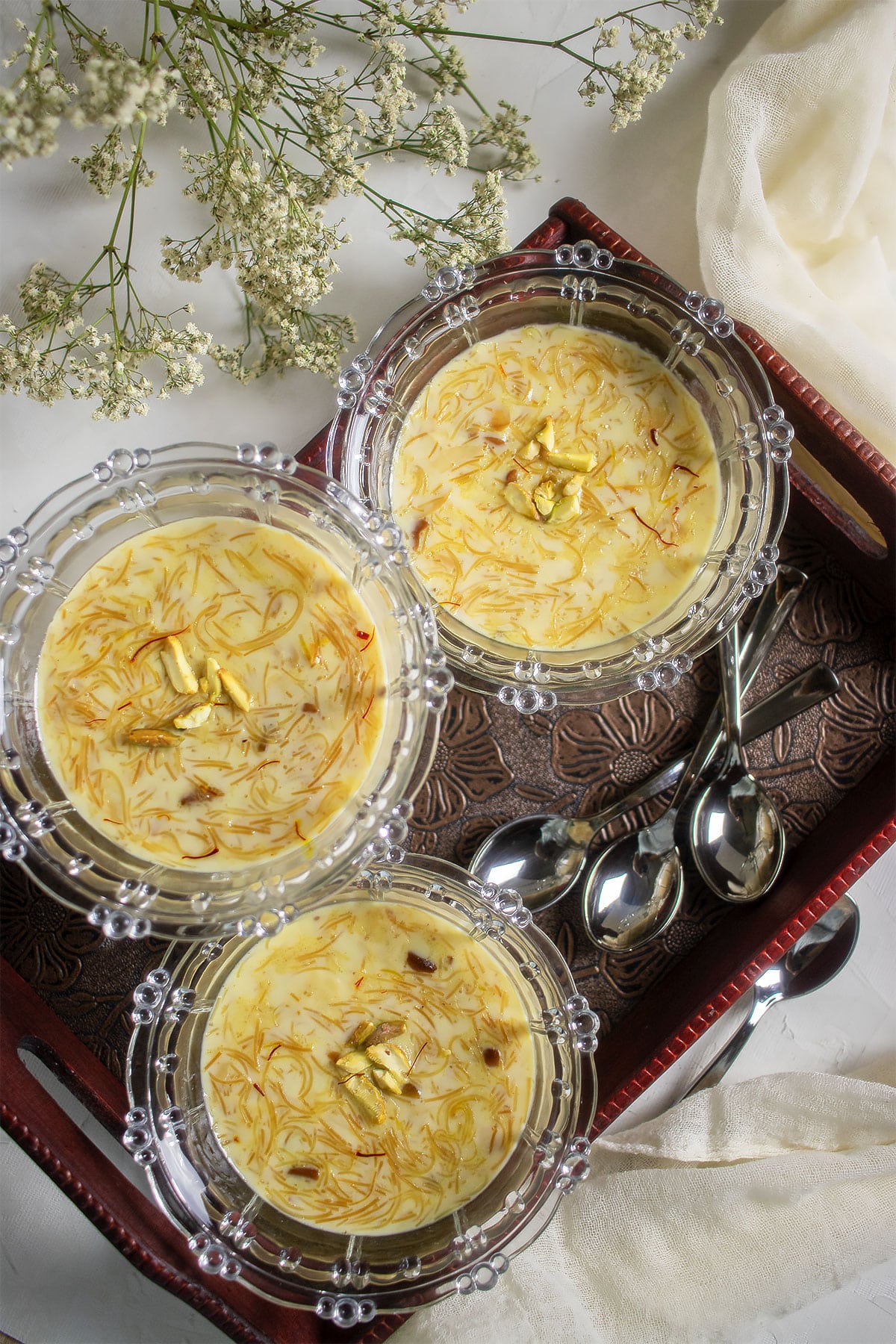 Three bowls of sheer khurma served in bowls over a serving tray.