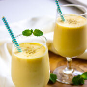 Mango lassi served in glasses with a sprinkle of cardamom powder.