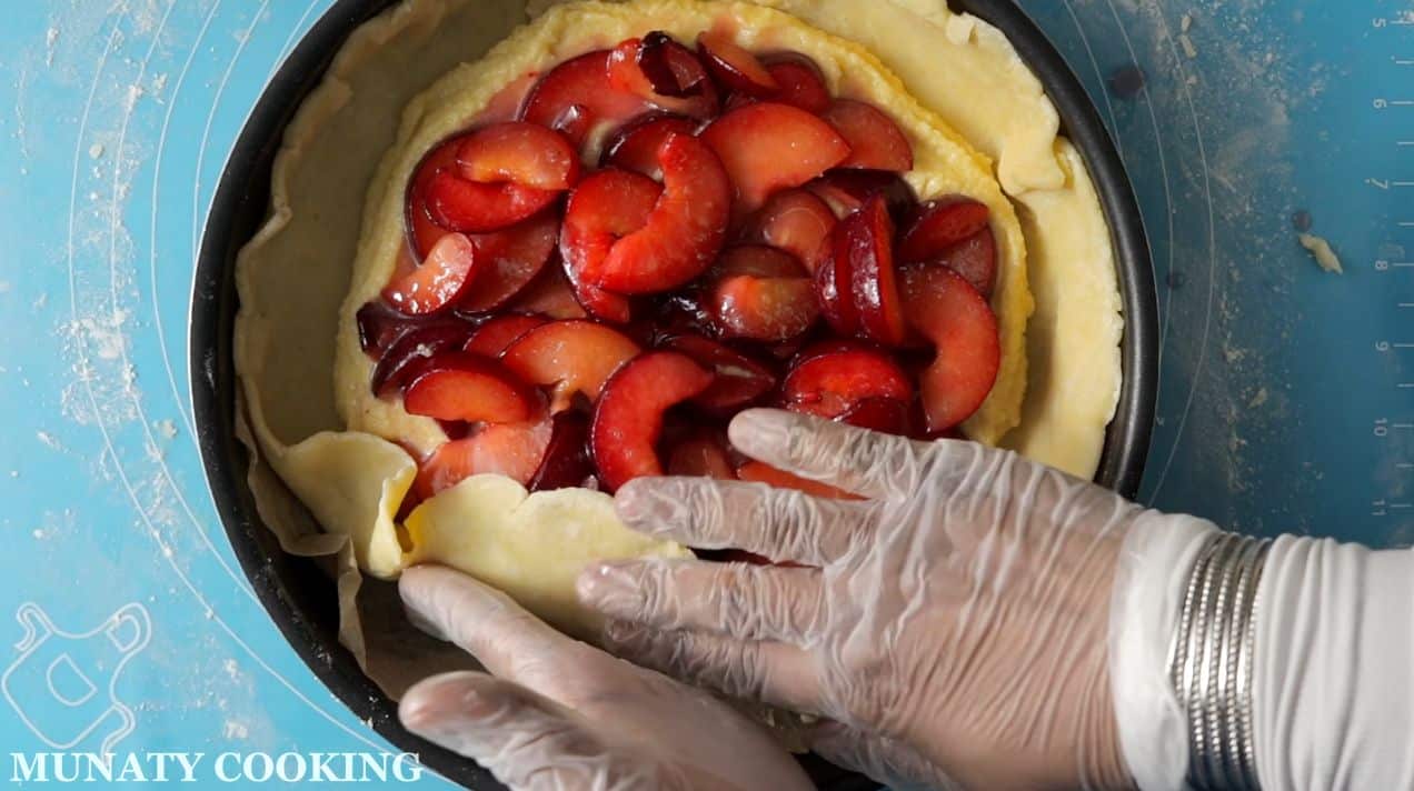 Folding the pie crust over the plum slices.