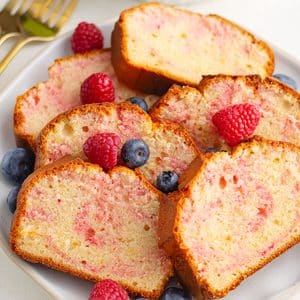Raspberry swirl cake slices on a white plate garnished with fresh raspberry.