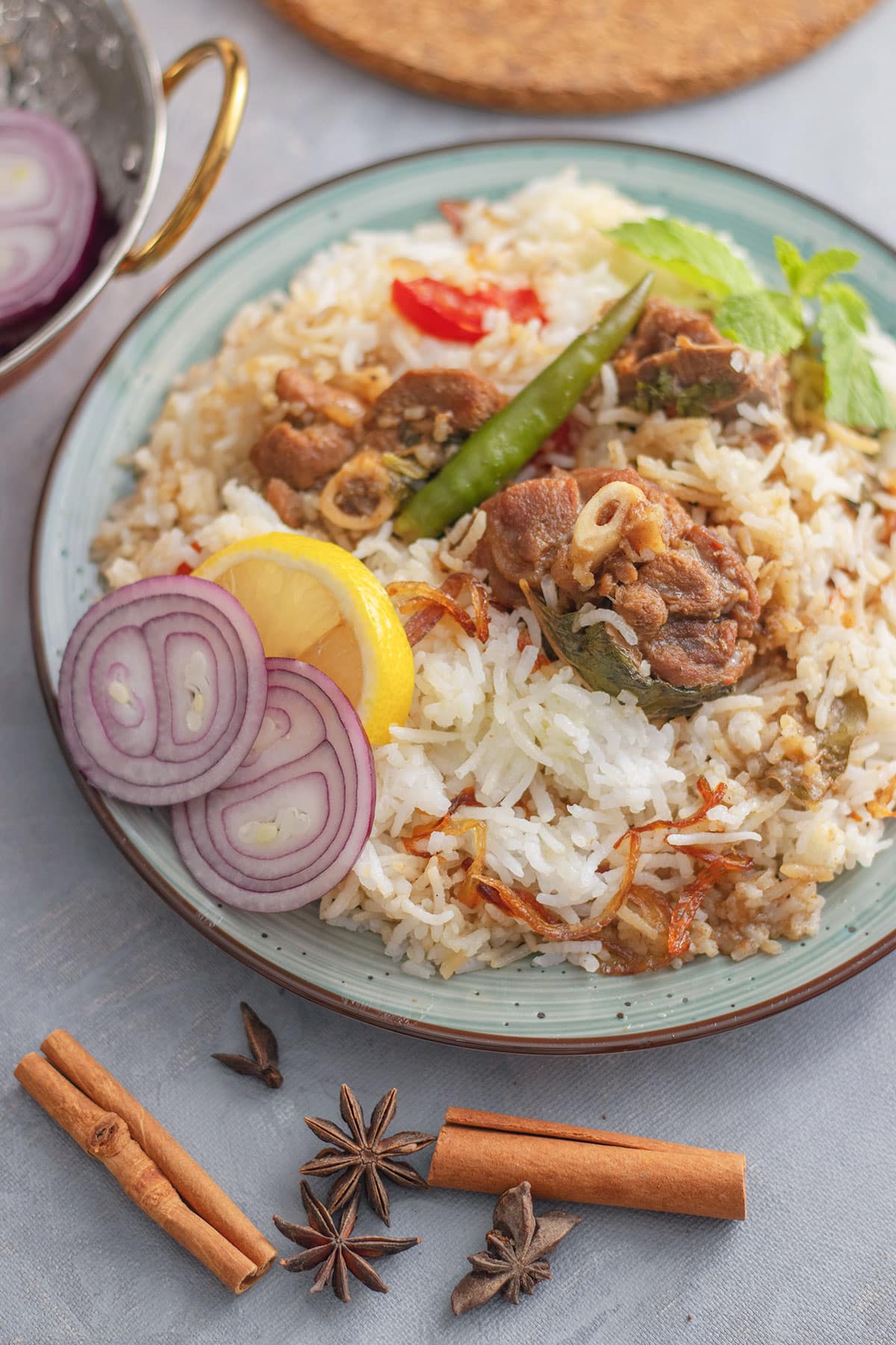 White mutton biryani served on a plate, garnished with slices of lemon and onion on the side.