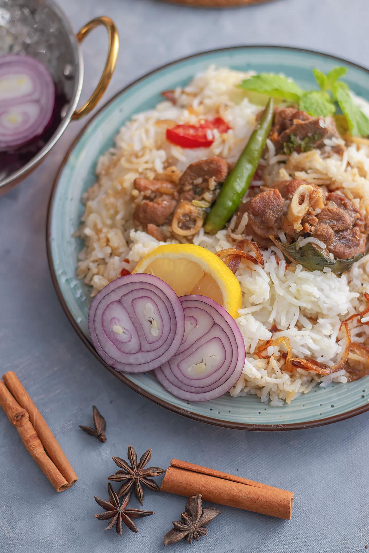 Showing mutton biryani, in a plate with lemon slice and onion slices on the side with fluffy white rice.